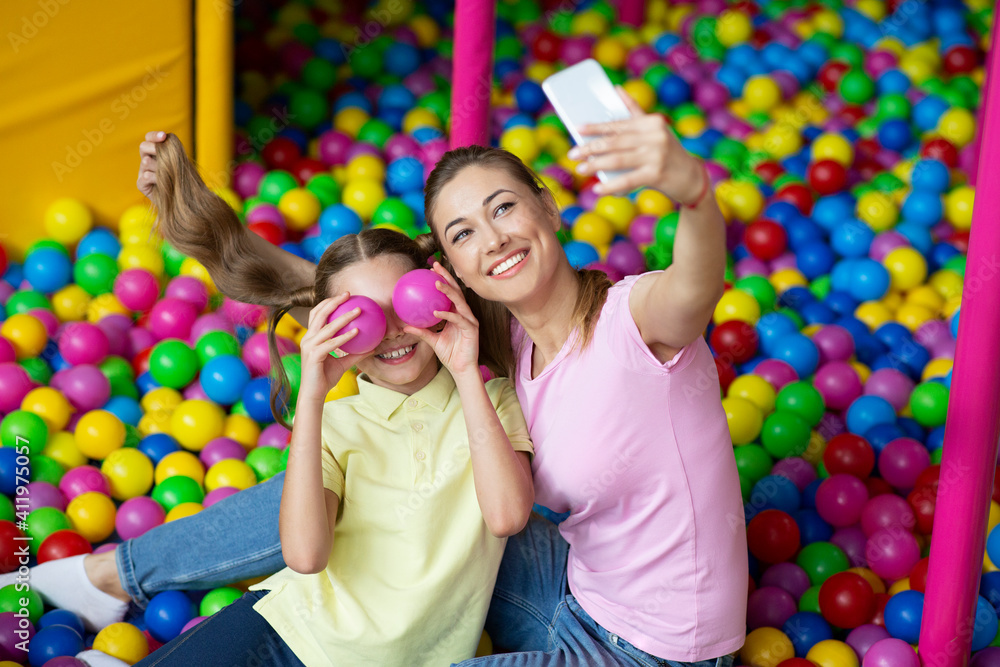 Mother and daughter taking a selfie while playing in a colorful ball pit